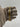 A two-tone gold and silver metal watch band held by a hand wearing a taupe glove, shown against a neutral light gray background.